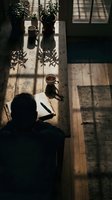 Person working at wooden desk with potted plants and coffee cup, overhead view with natural window light casting shadows, suitable for creative workspace and productivity concepts.