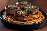 Grilled beef tenderloin medallions topped with fresh herbs and spices, served on a bed of glazed carrot strips in cast iron pan. Restaurant quality gourmet meal.