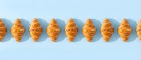 Freshly baked croissants arranged in a row on light blue background, perfect for bakery, food, and culinary design projects.