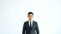 Young Asian male professional in dark business suit and blue tie standing against white background, isolated for corporate headshot and business portrait use.