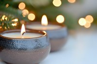 Lit candles in glittery containers with warm bokeh lights and evergreen branches, creating a cozy holiday ambiance for seasonal decorating and festive celebrations.