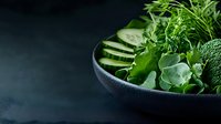 Fresh green vegetables and herbs in dark ceramic bowl on slate background for healthy cooking and nutrition concepts.