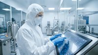 Scientist in protective suit working with touchscreen computer in sterile pharmaceutical laboratory for medical research and drug development.