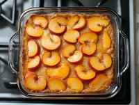 Fresh peach slices arranged in caramelized syrup within glass baking dish, showing vibrant orange fruit and golden brown caramel sauce on stovetop.