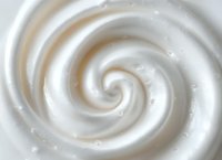 Creamy white swirl texture with soft spiral pattern creates luxurious cosmetic or dessert background, macro photography shows smooth whipped consistency.