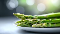 Fresh green asparagus spears arranged on white plate with soft bokeh background, macro food photography highlighting natural texture and vibrant color.