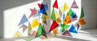 Colorful paper triangles in various sizes and hues scattered on white surface with dramatic shadows. Geometric shapes create vibrant abstract composition for creative projects.
