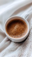 Fresh hot chocolate with tiny bubbles in white ceramic cup on cozy knitted fabric, top view close-up shot with soft morning light and gentle tones.