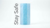 Blue disposable medical face mask standing upright on white background with Stay Safe text, health protection concept.
