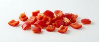Fresh red bell pepper pieces chopped and scattered on white background, isolated vegetable ingredient for cooking and culinary preparations.