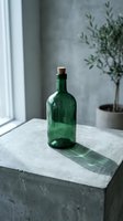 Empty green glass bottle with cork stopper on concrete surface near window with potted plant, suitable for beverage, potion, or home decor design projects.