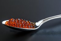 Fresh red caviar on silver spoon against dark background, gourmet seafood delicacy with translucent salmon roe pearls showing natural texture and shine.