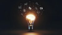 Glowing light bulb with business icons floating above on dark background representing innovation, creativity and entrepreneurial ideas for success.
