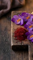 Saffron spice threads with purple crocus flowers on rustic wooden board, aromatic culinary ingredient for gourmet cooking and natural food photography.