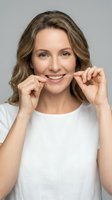 Middle-aged woman with shoulder-length brown hair and fair complexion flossing teeth against neutral background. Dental hygiene and oral care concept for healthcare and wellness marketing.