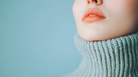 Close up of young Asian woman's face showing natural coral lips and pale skin wearing cozy gray turtleneck sweater against turquoise background.