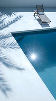 Luxury poolside scene with wooden lounge chair and palm tree shadows on white deck. Crystal clear blue water reflects bright sunlight creating serene vacation atmosphere.