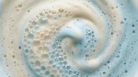 Creamy white foam with swirling blue tones and tiny bubbles, creating a soft abstract texture for backgrounds, packaging, and spa designs.