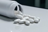 White pharmaceutical pills scattered from prescription bottle on light surface, selective focus with shallow depth of field for medical and healthcare concepts.