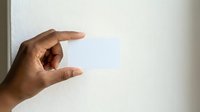 Hand holding blank white card or paper against neutral wall background, suitable for mockup, branding, advertising, and presentation purposes.