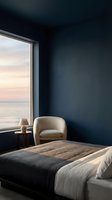 Minimalist bedroom with dark blue walls, cream armchair, wooden side table, and large window overlooking serene ocean at sunset, ideal for interior design and hospitality projects.
