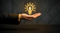 Businessman hand holding glowing lightbulb with cross symbol, representing innovation, faith, and spiritual enlightenment for business and religious concepts.