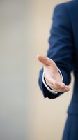 Professional businessman in navy suit extending open hand in welcoming gesture for business meetings, partnerships, negotiations, and corporate communication concepts.