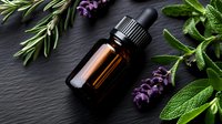 Amber glass essential oil bottle with dropper surrounded by fresh aromatic herbs - lavender, rosemary and sage leaves on dark stone background. Natural aromatherapy concept.