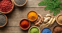 Colorful superfood ingredients in wooden bowls on rustic table including goji berries, chia seeds, turmeric, spirulina powder and fresh moringa leaves for healthy cooking.