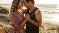 Young couple embracing intimately on beach at sunset, romantic moment with ocean waves in background, love and connection concept for lifestyle content.