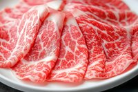 Fresh marbled beef slices arranged on white plate showing premium meat texture and distinctive fat marbling pattern characteristic of high-grade beef.