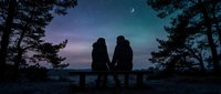 Couple sitting on bench at twilight surrounded by pine trees with crescent moon in starry sky, romantic evening scene for relationships and love concepts.
