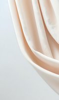 Soft flowing cream-colored fabric creates gentle folds and curves against white background, offering minimalist elegance for fashion and interior design projects.
