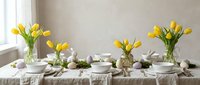 Elegant Easter table setting with yellow tulips, decorated eggs, and white dinnerware on linen tablecloth for spring holiday celebration and dining.