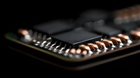 Close-up macro shot of electronic circuit board components with copper contacts and black microchip in dramatic lighting, showing technology detail and precision.