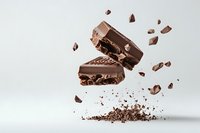 Broken dark chocolate bar with nuts floating in air against light background, dynamic food composition with scattered pieces and crumbs in motion.