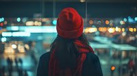 Young Asian woman in red beanie and dark coat looking at city lights at night, back view. Blurred urban bokeh creates dreamy atmospheric mood for lifestyle and travel concepts.