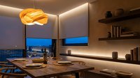 Modern dining room interior with wooden table, pendant lighting and city view through large windows at twilight for contemporary home design.