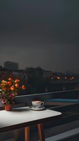 Cozy evening balcony scene with coffee cup and orange roses in terracotta pot against city twilight backdrop, creating atmospheric mood for relaxation.