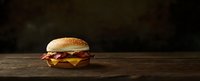 Bacon cheeseburger with melted cheese and crispy strips on rustic wooden table against dark background, dramatic food photography with copy space.