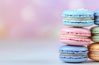 Colorful French macarons in pastel blue and pink stacked on white surface against soft blurred background, sweet dessert photography for bakery marketing.