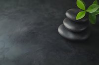Stacked black spa stones with fresh green leaves on dark textured background. Zen and wellness concept for spa, meditation, and relaxation practices.
