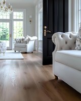 Bright luxury living room interior with white tufted armchairs, black door, crystal chandelier, hardwood flooring and large windows overlooking garden view.
