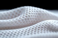 Soft white mesh fabric with honeycomb pattern creates gentle waves and folds against dark background, showcasing texture and depth in macro photography.