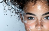 Close up portrait of young mixed race woman with natural curly hair and water drops on glass surface creating artistic reflection effect and texture.