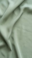 Soft sage green fabric with elegant draping and smooth texture creates luxurious flowing material for fashion and interior design projects.