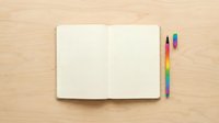 Open notebook with blank pages and colorful markers on wooden surface, ready for writing, planning, or creative projects.