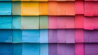 Vibrant rainbow colored wooden shingles on building exterior create gradient pattern from blue to pink, architectural detail shows weathered texture and overlapping design.