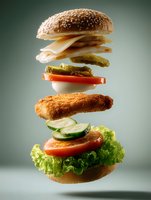 Deconstructed crispy chicken burger with fresh vegetables and sesame bun floating in air against gradient background. Creative food photography for restaurant menu.