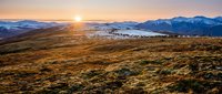 Golden sunrise over mountain landscape with rolling hills and distant snow-capped peaks creating dramatic natural scenery for outdoor adventure content.